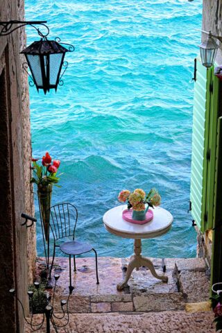 A table and chair by the ocean in between buildings in Ravanij, Croatia.