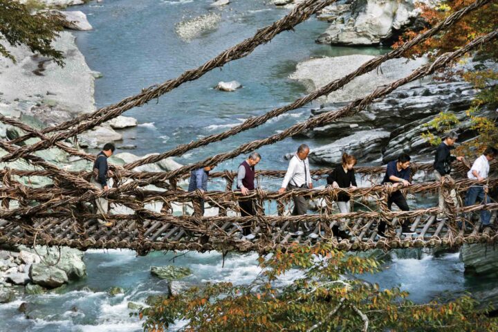 A group of tourists walking on a vine bridge over the Iya river.