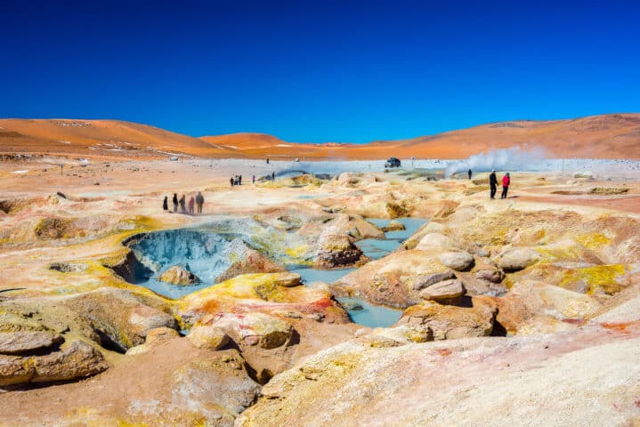 Huayllajc, Bolivia - August 25, 2015: Group of tourists looking at steaming hot water ponds and mud pots in geothermal region of